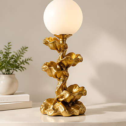 Globe table lamp with a gold-tone floral stem and sculptural flower-shaped base on a light tabletop