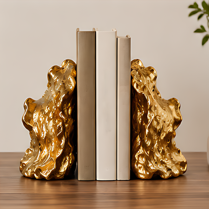 Two gold-tone sculptural bookends framing upright neutral-colored books on a wooden tabletop