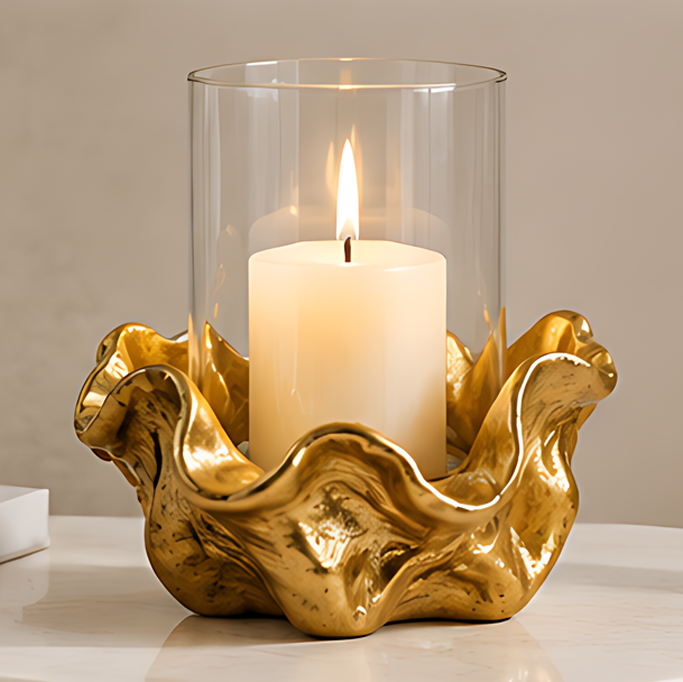 Gold-tone sculptural flower candle holder with a clear cylindrical glass shade displaying a lit white pillar candle