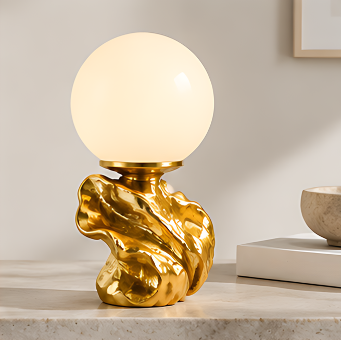 Glowing round globe table lamp on a sculptural gold-tone base displayed on a light tabletop